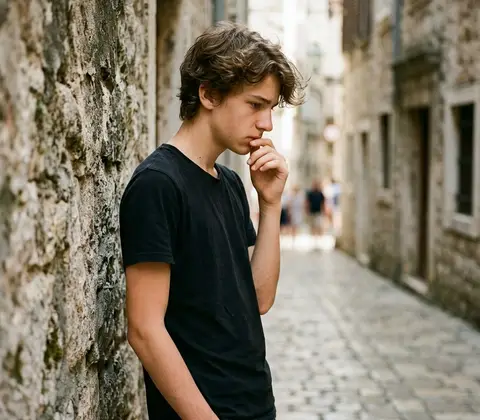 Jan, con camiseta negra, pensativo junto a una pared de piedra.