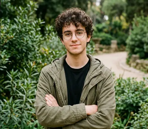 Nil, con gafas y chaqueta verde, de brazos cruzados en un parque.